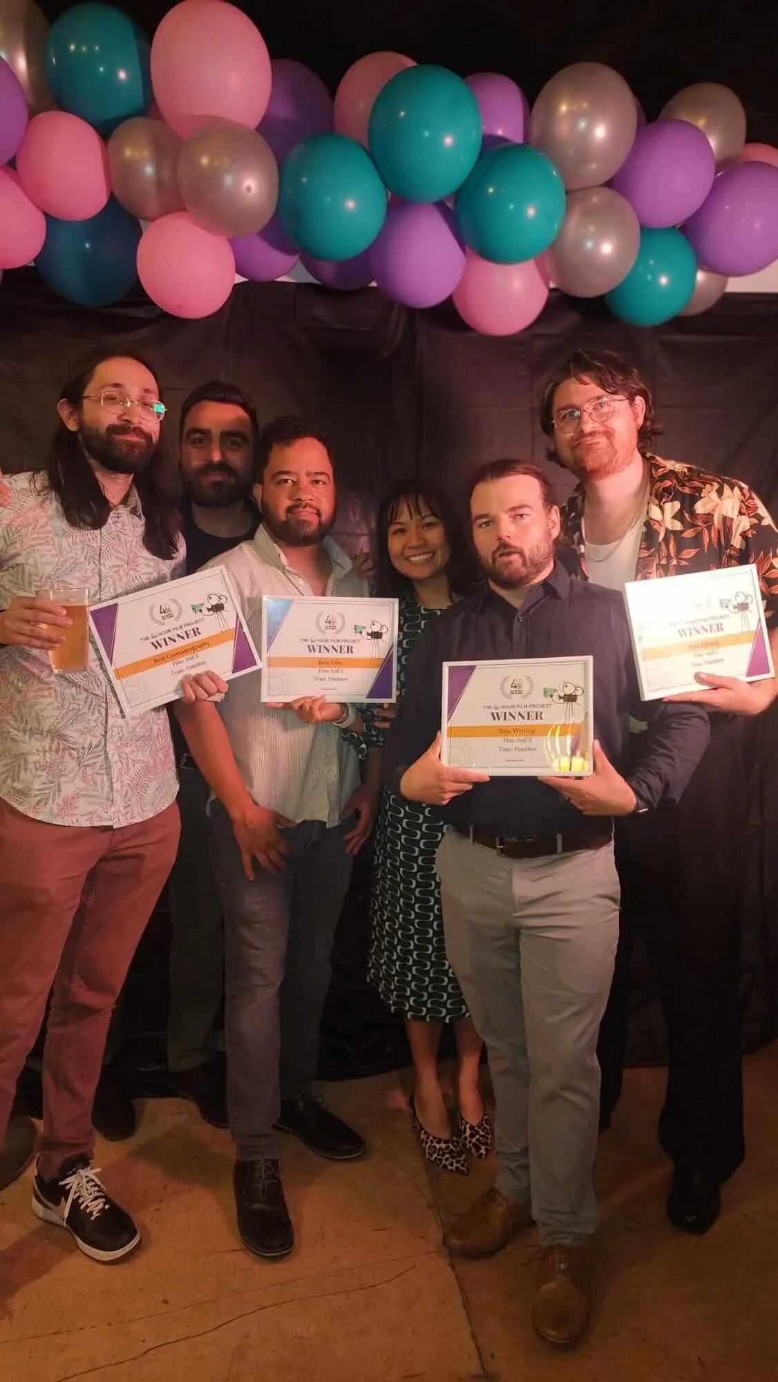 Six guests pose together holding framed film awards